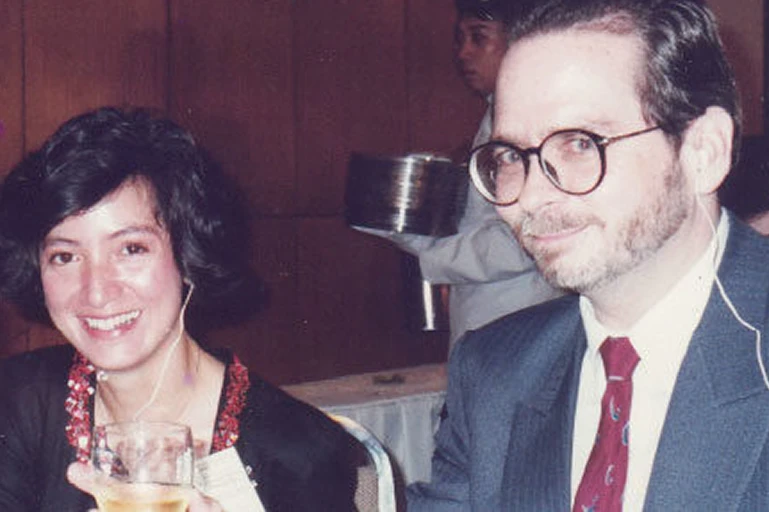 Our Story 1992 A smiling man with glasses in a suit sits beside a smiling woman at a formal event