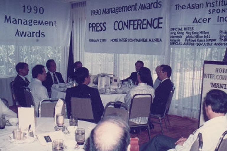 Our Story 1992 A smiling man with glasses in a suit sits beside a smiling woman at a formal event